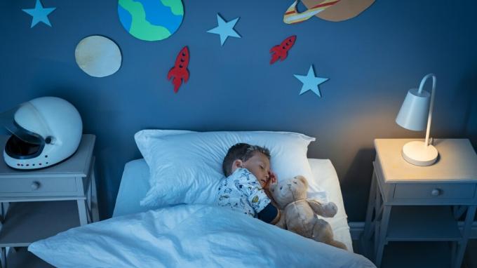 Wysoki kąt widzenia małego chłopca ADHD marzącego o zostaniu astronautą podczas snu z misiem w pokoju urządzonym w przestrzeni.